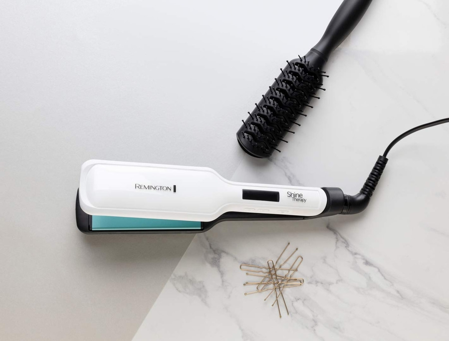 Haarglätter, Haarbürste und Haarnadeln auf Marmoroberfläche. Friseurwerkzeuge.