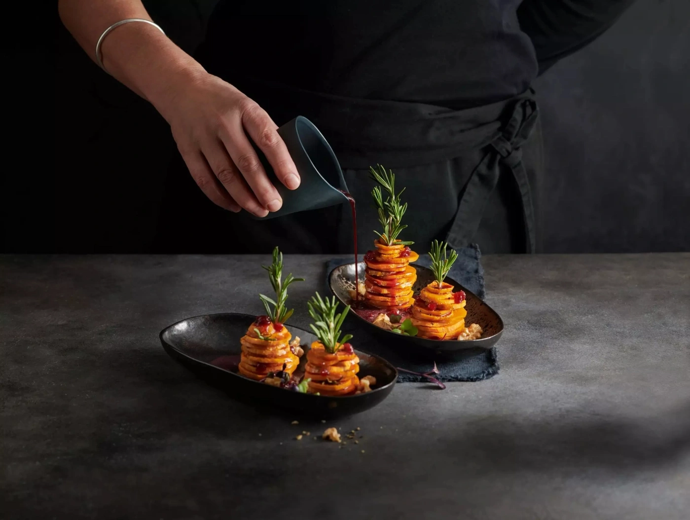 Ein Koch übergießt Süßkartoffel-Türmchen mit Sauce.