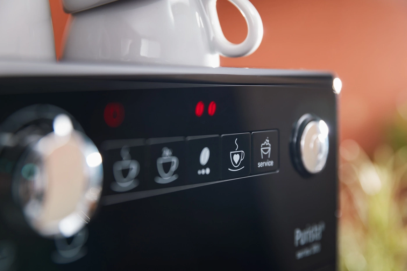 Nahaufnahme einer Kaffeemaschine mit roten Lichtern und Symbolen für Kaffeezubereitung und Service.