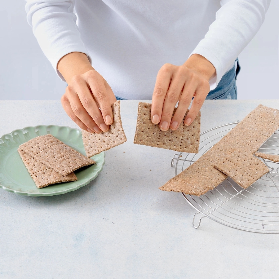 Person bricht Knäckebrot in der Hand, auf Teller und Rost