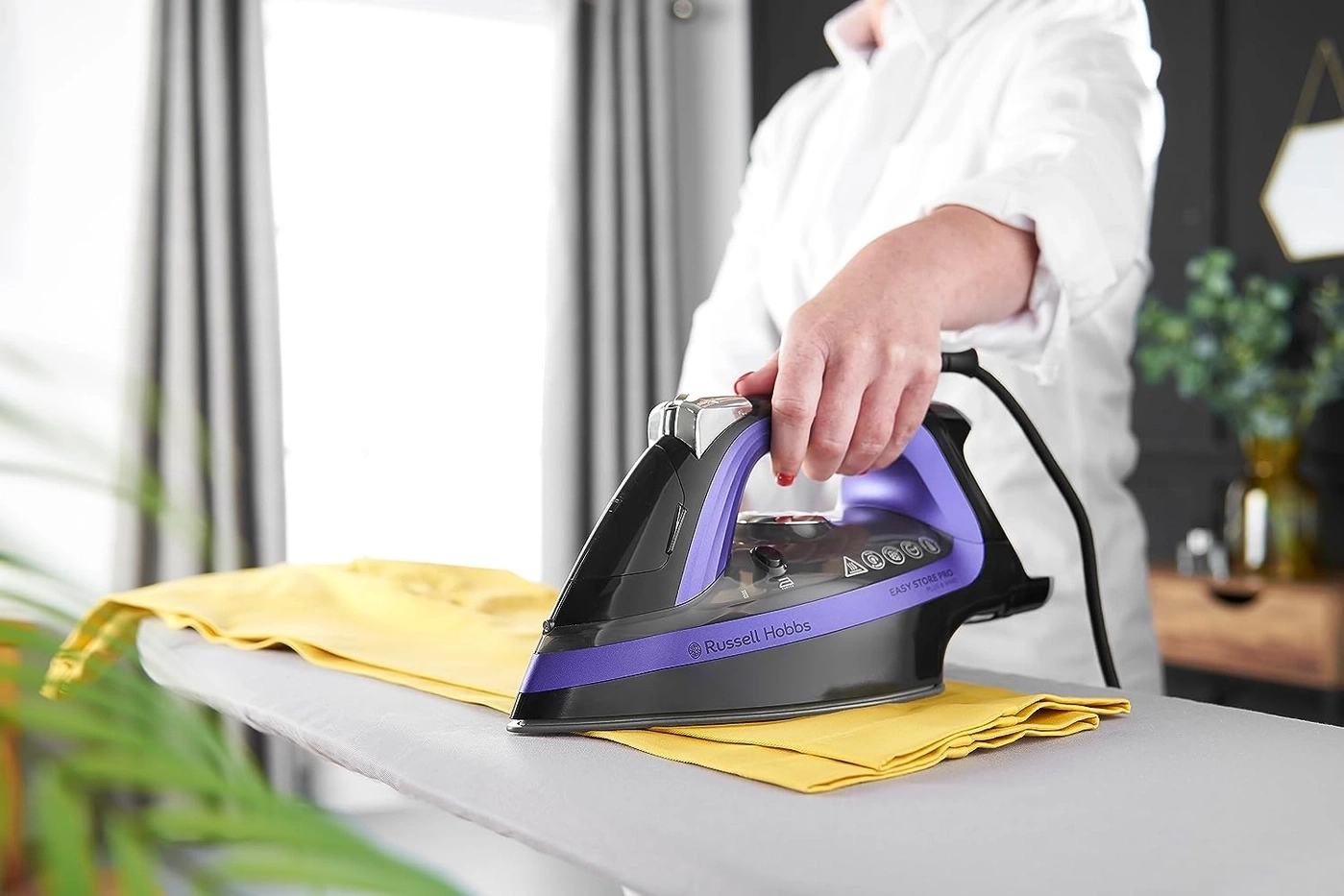 Person bügelt gelbes Kleidungsstück mit einem Bügeleisen auf einem Bügelbrett