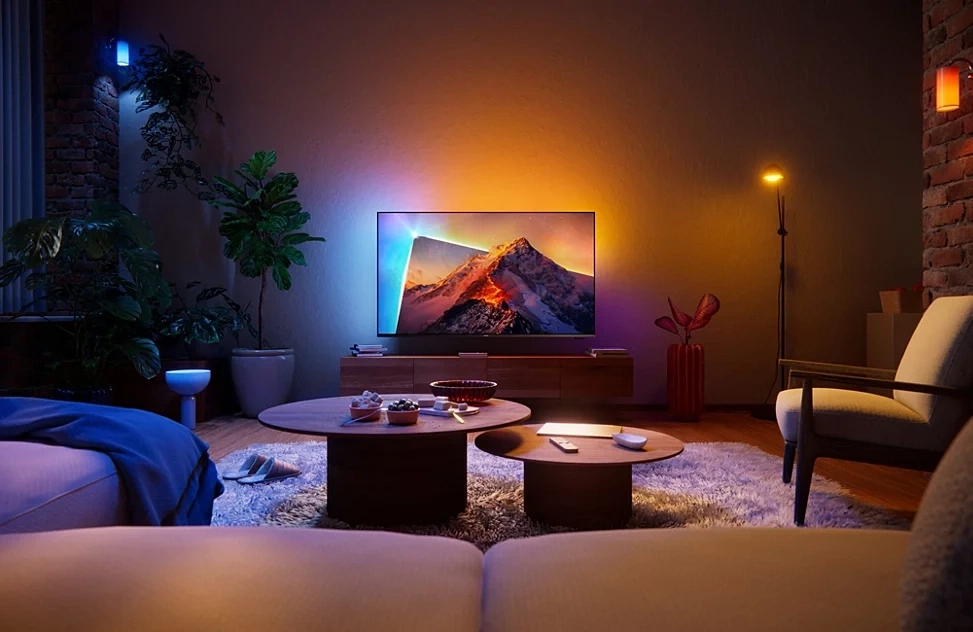 Ein gemütliches Wohnzimmer mit einem großen Fernseher, der ein Bergpanorama zeigt und stimmungsvoller Beleuchtung.