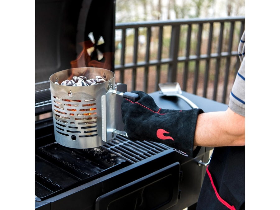 Person mit Grillhandschuh hält einen glühenden Kohleanzünder am Grill.