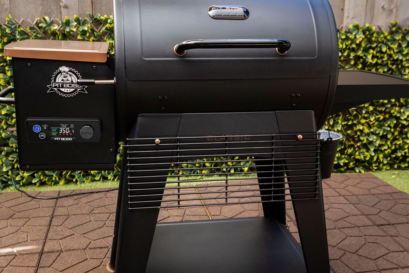 Ein schwarzer Pit Boss Grill mit digitaler Anzeige und Kupferakzenten steht auf einer gepflasterten Terrasse.
