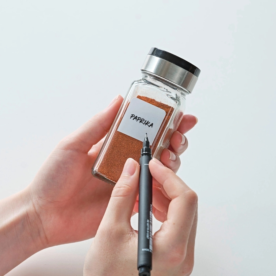Person beschriftet ein Gewürzglas mit Paprika, Nahaufnahme, Hände, Stift, Etikett