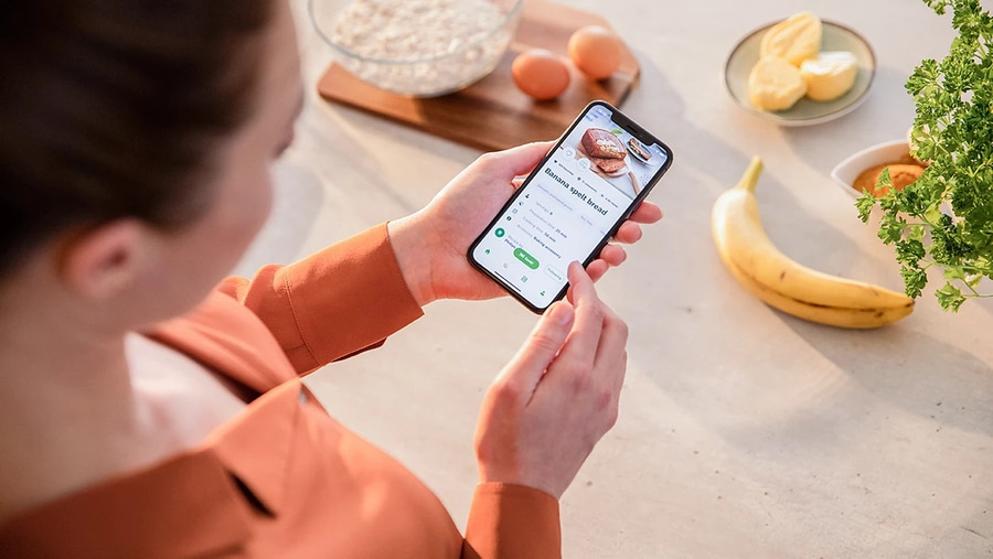 Person mit Smartphone in der Hand, Kochrezept für Bananenbrot