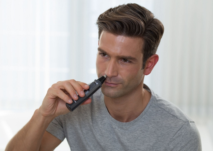 Mann rasiert sich die Nase mit einem elektrischen Trimmer. Nahaufnahme.