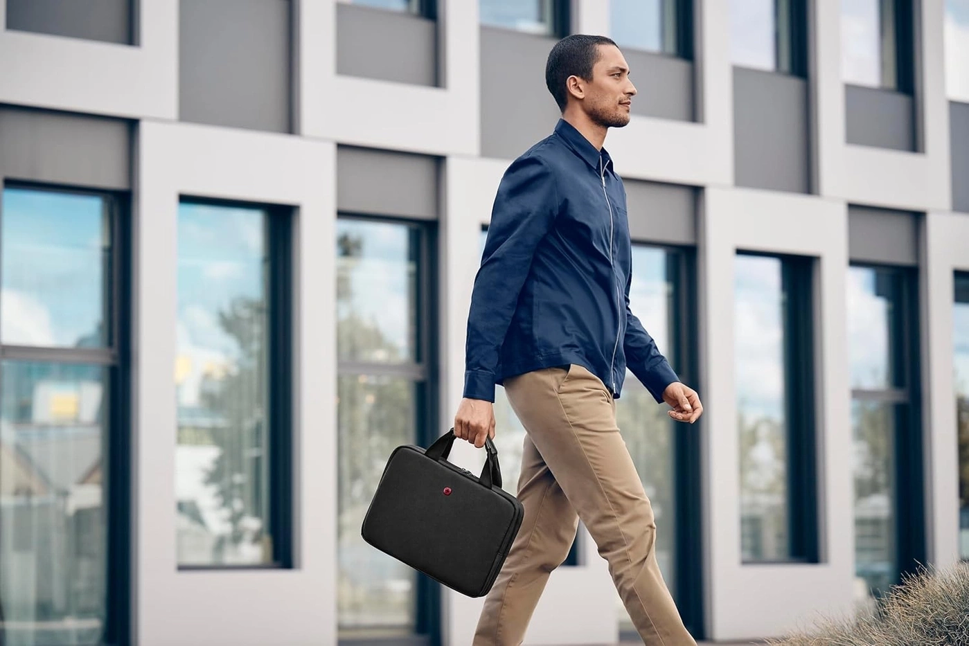 Mann mit schwarzer Tasche geht an einem Gebäude vorbei, blaues Outfit