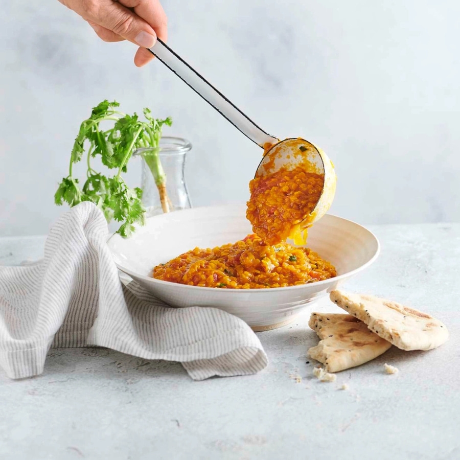Linsen-Curry wird mit einer Schöpfkelle in eine Schüssel gegeben, mit Brot.