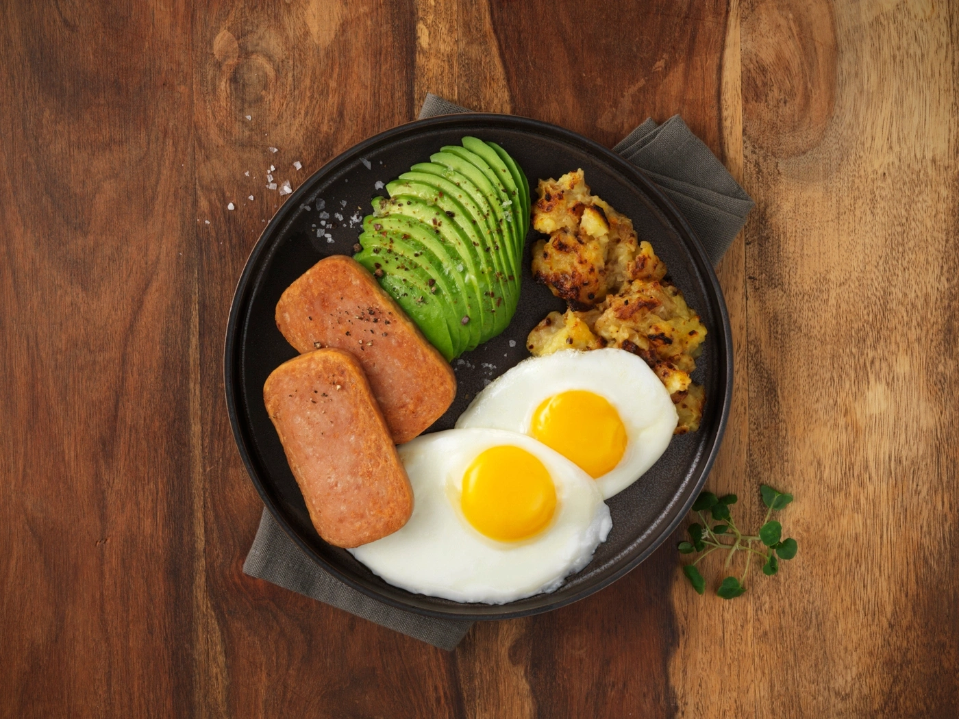 Frühstücksteller mit Spiegeleiern, Avocado, gebratenem Spam und Hash Browns.