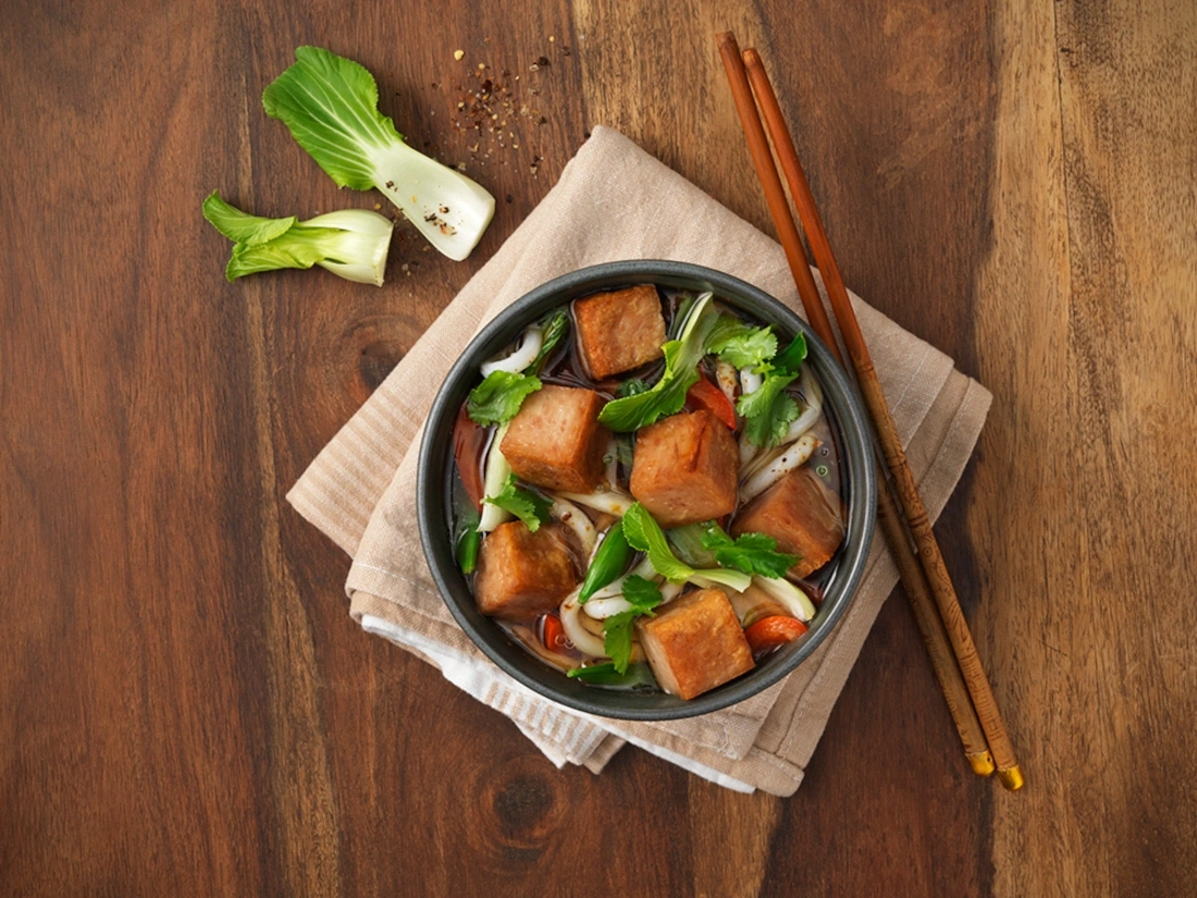 Ein Schüssel mit asiatischem Essen, Tofu und Gemüse auf einem Holztisch mit Stäbchen