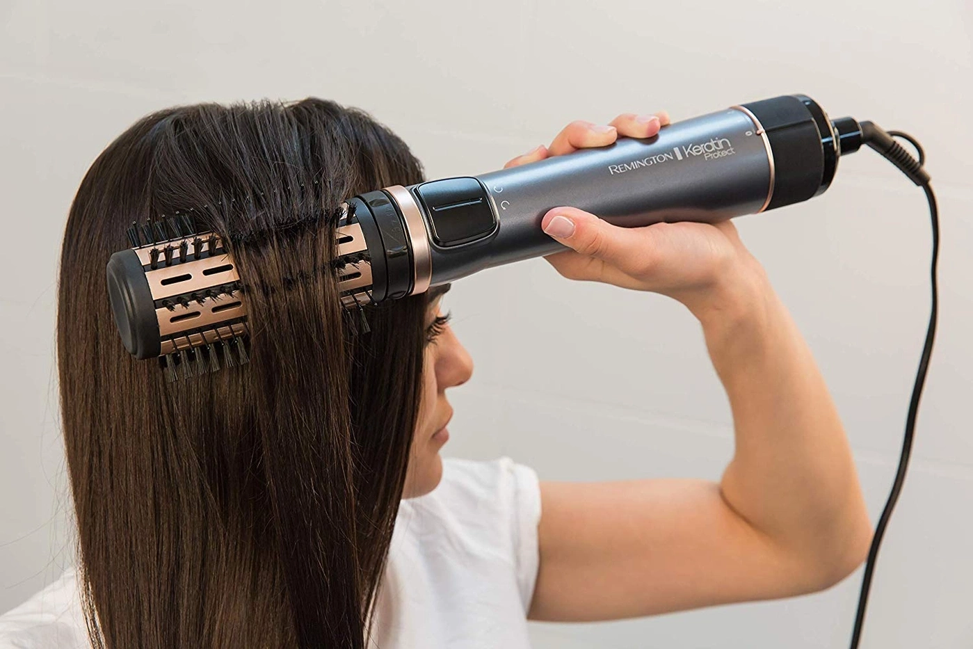 Frau benutzt einen Haartrockner, um ihre Haare zu stylen. Das Gerät ist von Remington.