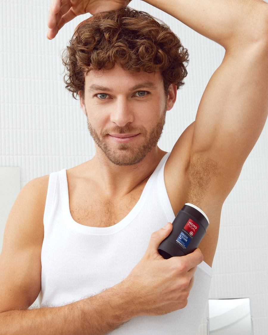 Mann mit Deodorant, hebt Arm, Blick in die Kamera, weißes Tanktop