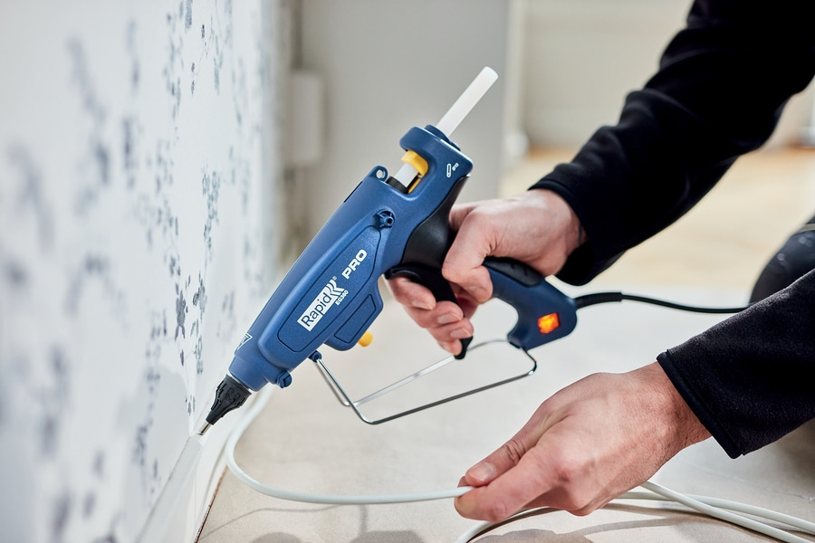 Hand mit Klebepistole repariert eine Wandleiste