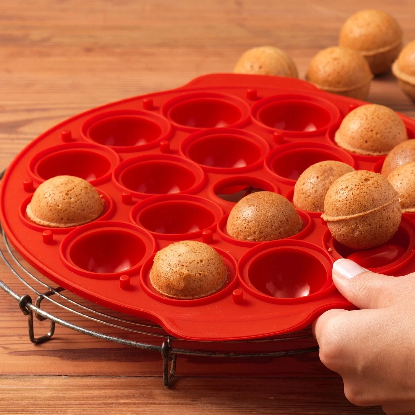 Roter Kuchenbackform mit kleinen Kuchen, die von einer Hand gehalten werden.