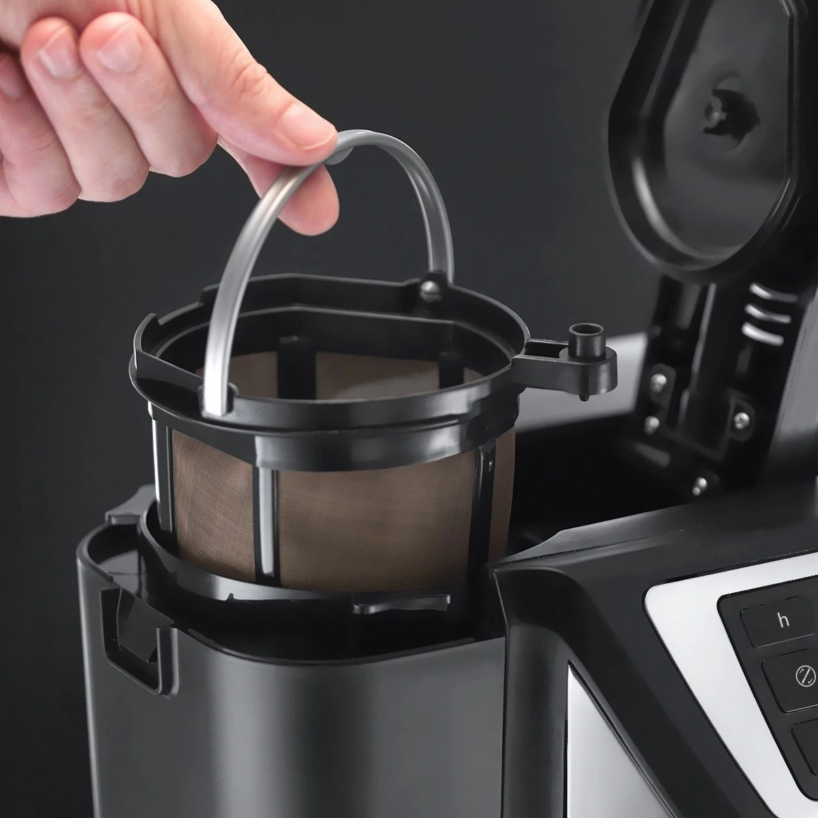 Hand hält Kaffeefilter mit Griff aus Metall in Kaffeemaschine