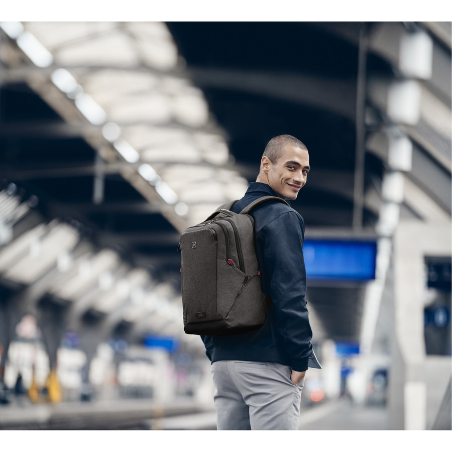 Mann mit Rucksack, der sich auf einem Bahnhof umschaut und lächelt.