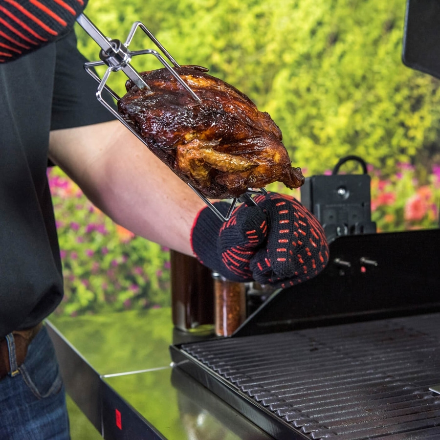 Gebratene Hähnchen auf dem Grill, gehalten von einer Person mit Ofenhandschuhen.