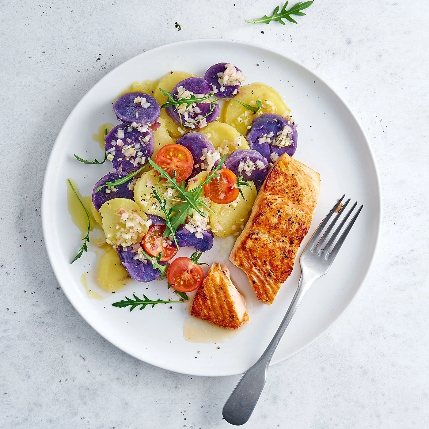 Teller mit Lachs, Kartoffelsalat und Tomaten, serviert auf einem weißen Teller