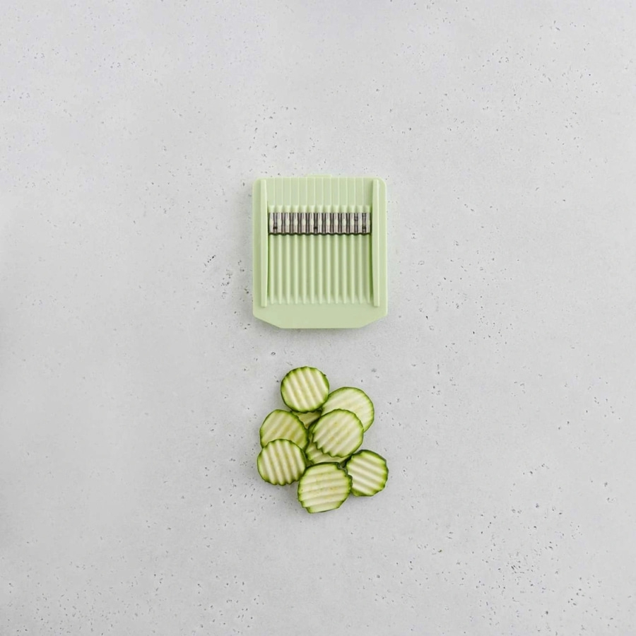 Gurkenscheiben und ein grüner Gemüseschneider auf grauem Hintergrund.