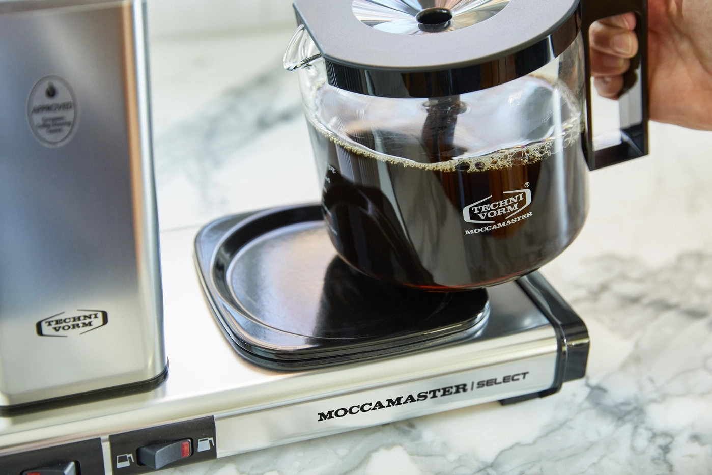 Kaffeemaschine mit Kaffeekanne, gefüllt mit Kaffee, auf einer weißen Oberfläche.