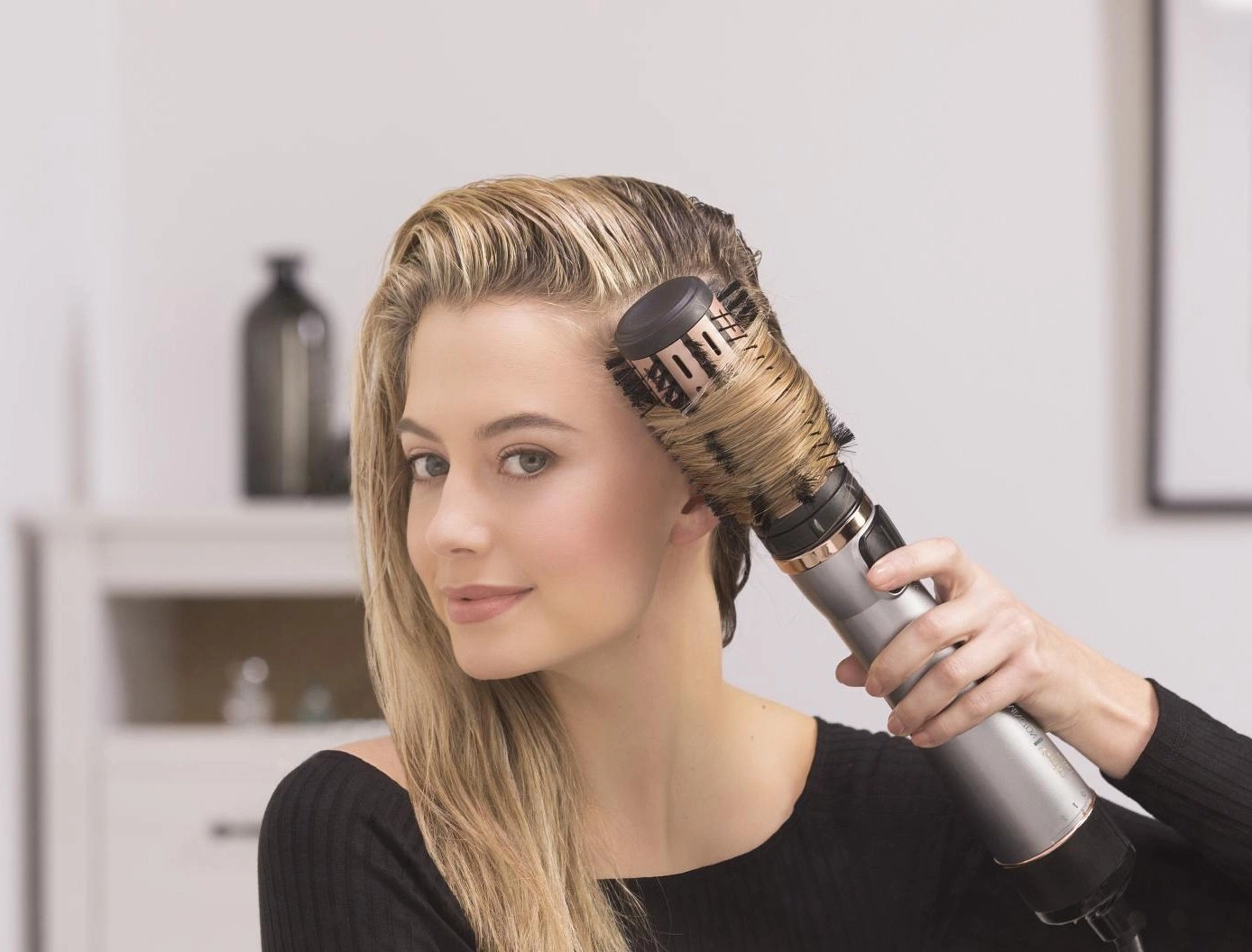 Frau föhnt sich die Haare mit einer Rundbürste, Blick in die Kamera