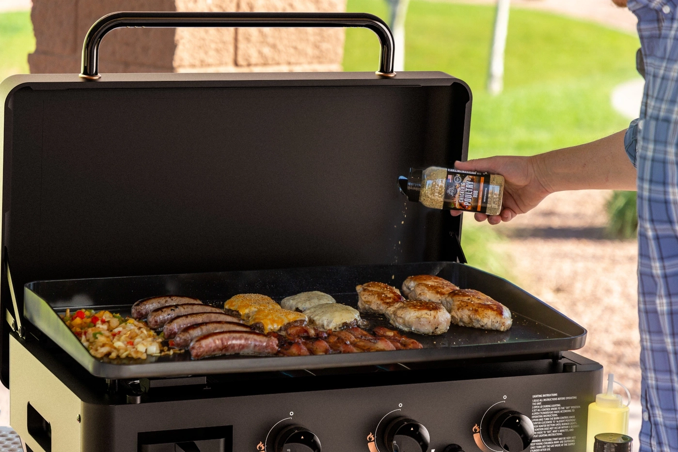 Person würzt Hähnchen und Würstchen auf einem Grill.