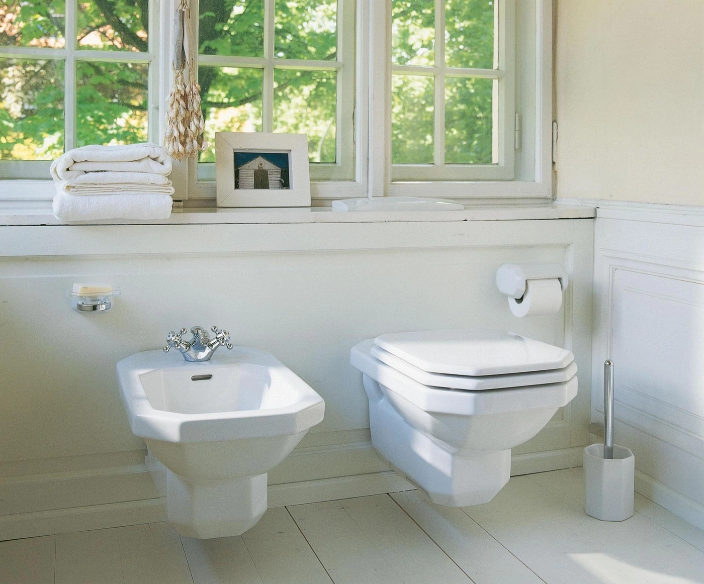 Weißes Badezimmer mit Fenster, Toilette, Bidet, Handtüchern und Dekoration.