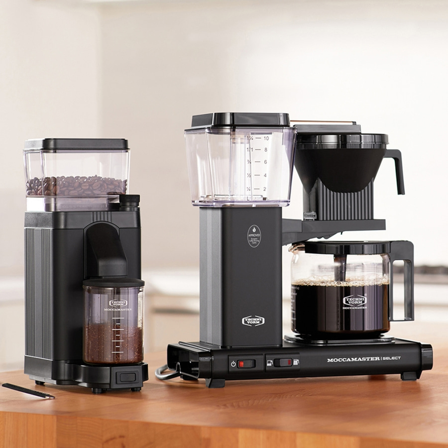 Schwarze Kaffeemaschine und Kaffeemühle auf Holzoberfläche, Nahaufnahme.
