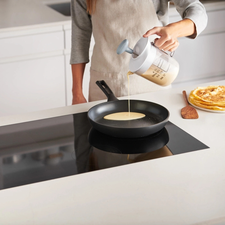 Person gießt Teig in eine Pfanne, um Pfannkuchen zu machen.