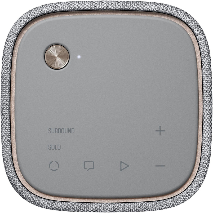 Grauer Lautsprecher mit Knöpfen und Text, der von einem Stoff umgeben ist.