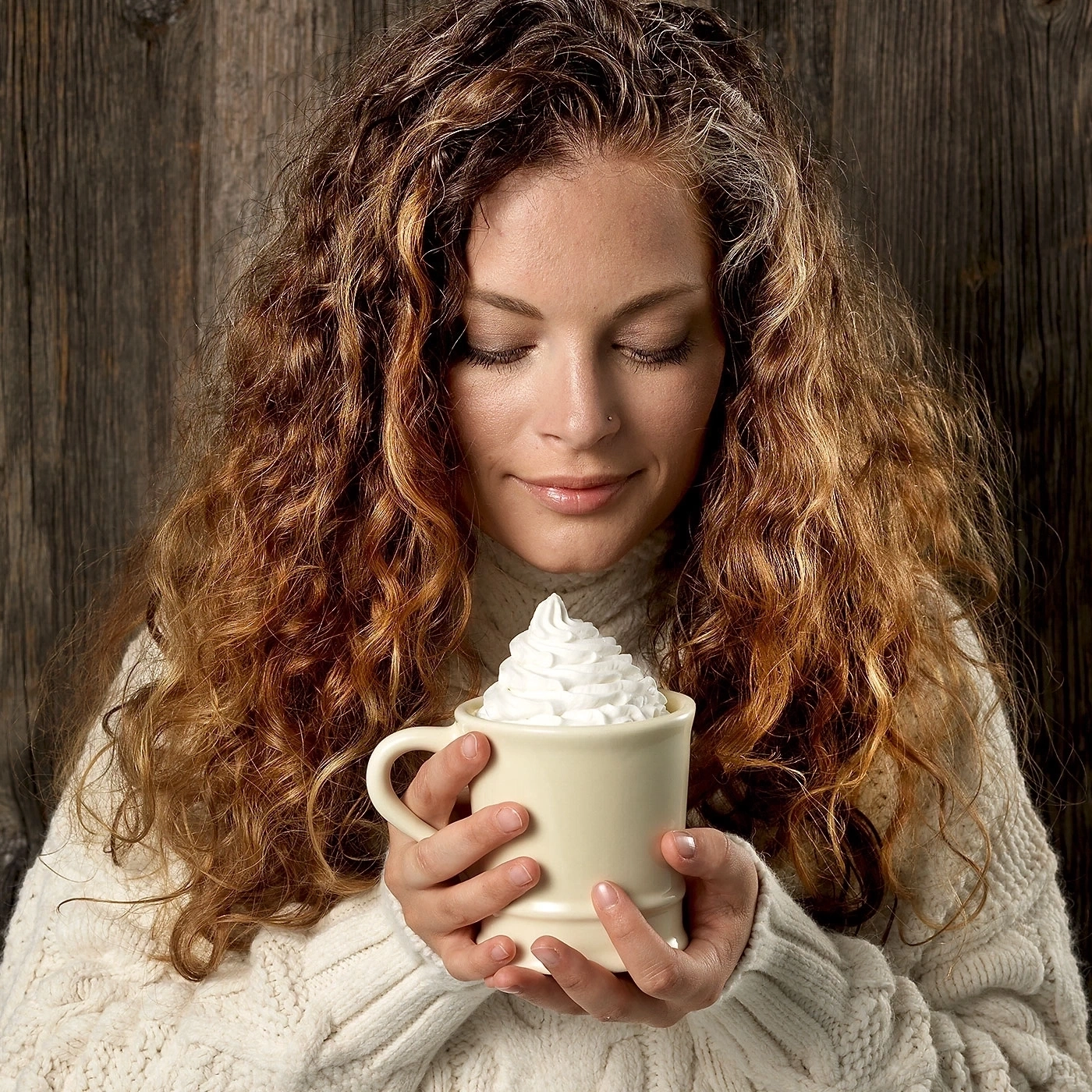 Frau mit lockigem Haar hält eine Tasse mit Sahne, lächelt, Holz Hintergrund