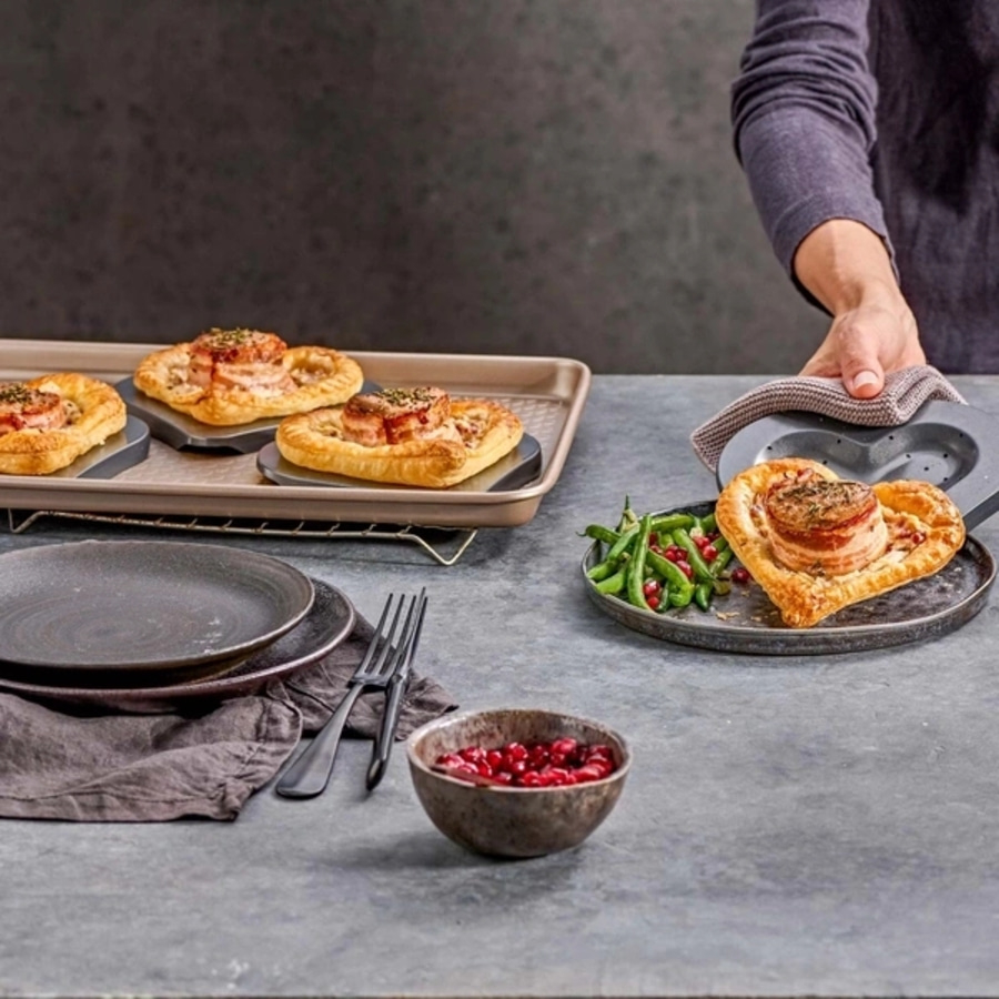Herzförmiges Gericht mit Beilagen, serviert auf einem Teller, mit Besteck und einer Schüssel.