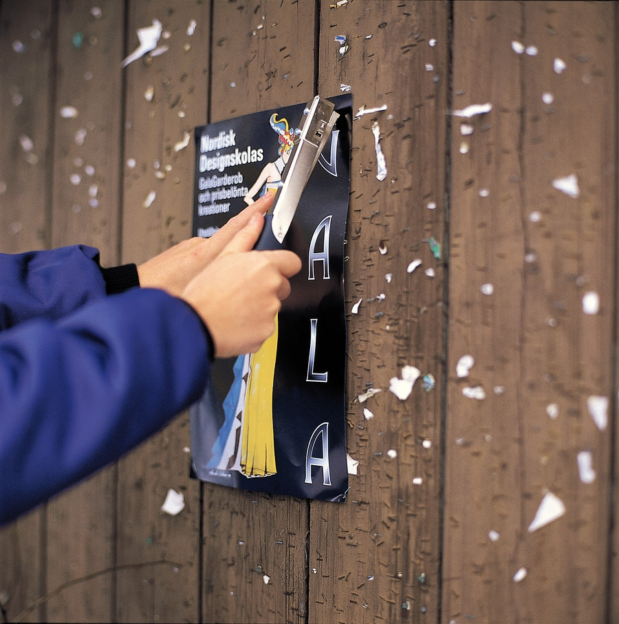 Person reißt Poster von Holzwand ab, Stapler mit Hebeklinge sichtbar.