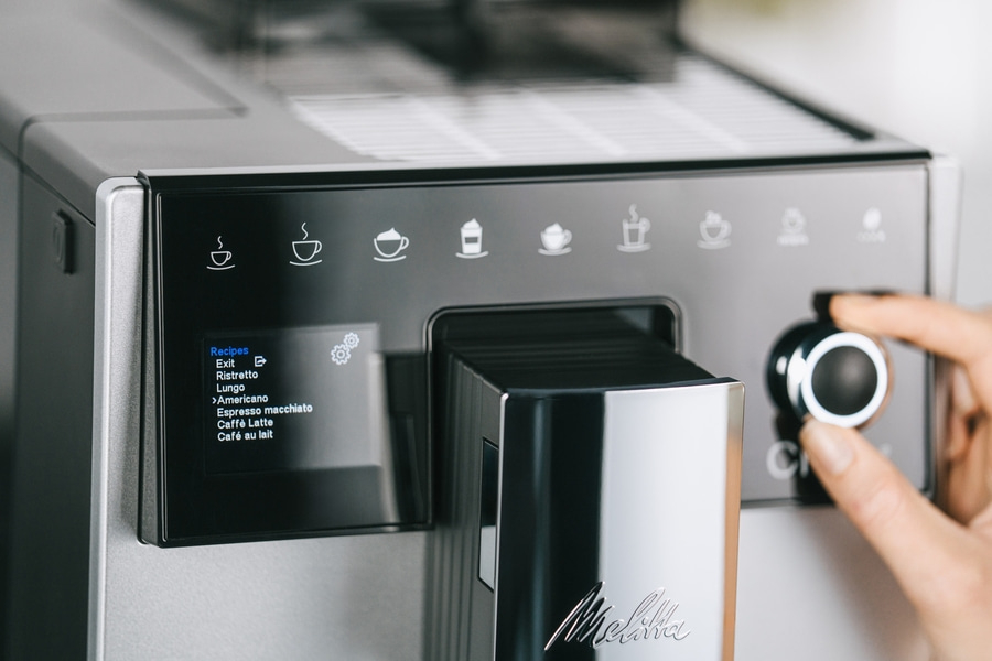 Kaffeemaschine mit Menüauswahl und Drehknopf. Melitta-Logo. Auswahl: Americano, Espresso macchiato, Caffè Latte.