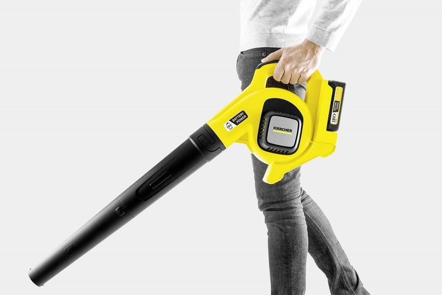 Person hält gelben Laubbläser. Kärcher-Logo und 18V-Batterie. Schwarzer Auslass.