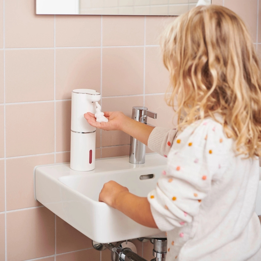 Ein Kind benutzt einen Seifenspender über einem Waschbecken im Badezimmer.