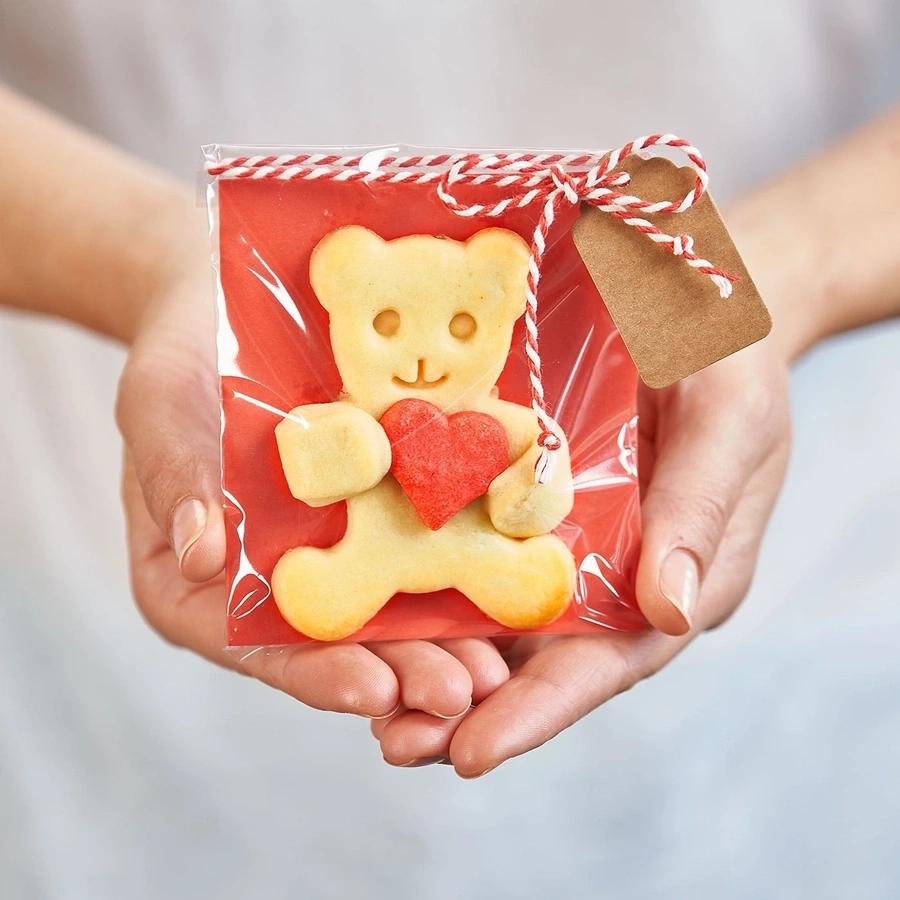 Teddybär-Keks mit Herz in Geschenkverpackung, gehalten von Händen