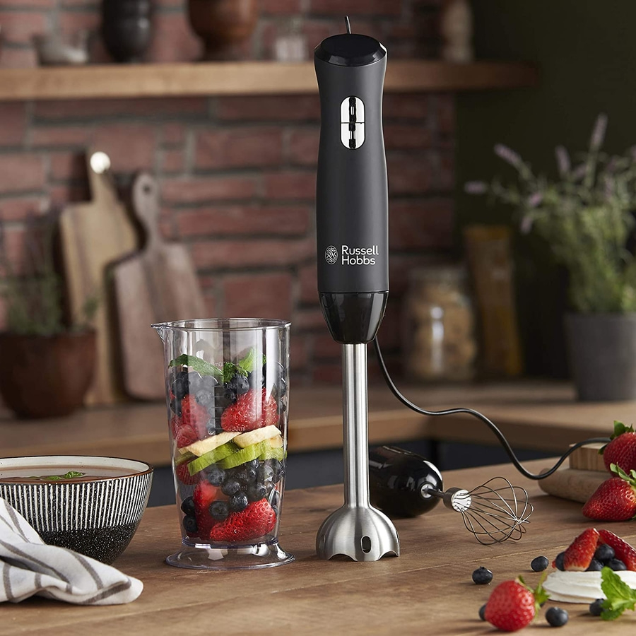 Schwarzer Stabmixer mit Beeren und Obst in einem Glas auf einem Holztisch.
