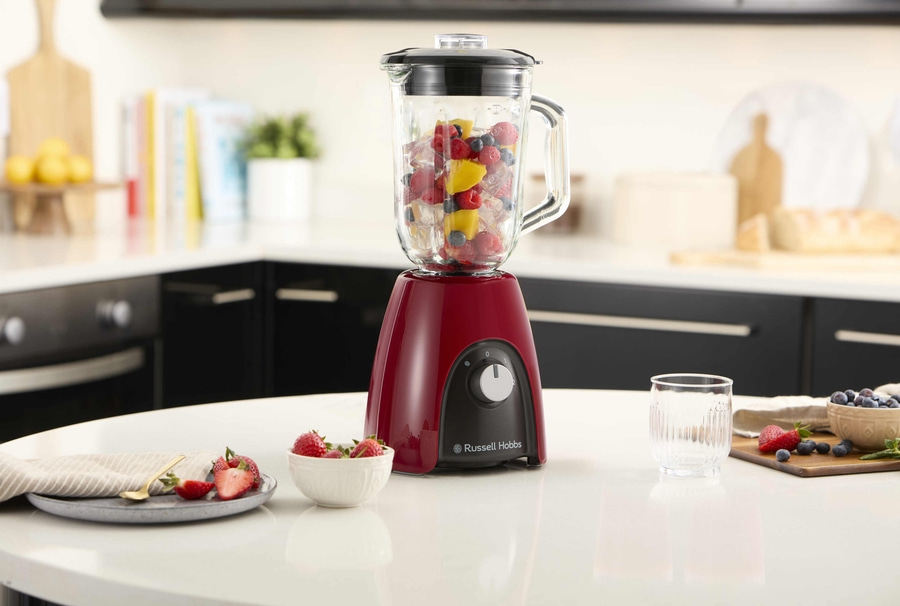 Ein roter Mixer mit Früchten, Erdbeeren und Blaubeeren auf einem Tisch in der Küche.