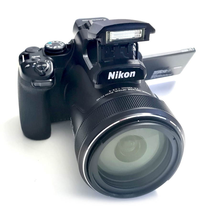 Nikon Digitalkamera mit ausklappbarem Blitz und Zoomobjektiv auf weißem Hintergrund.
