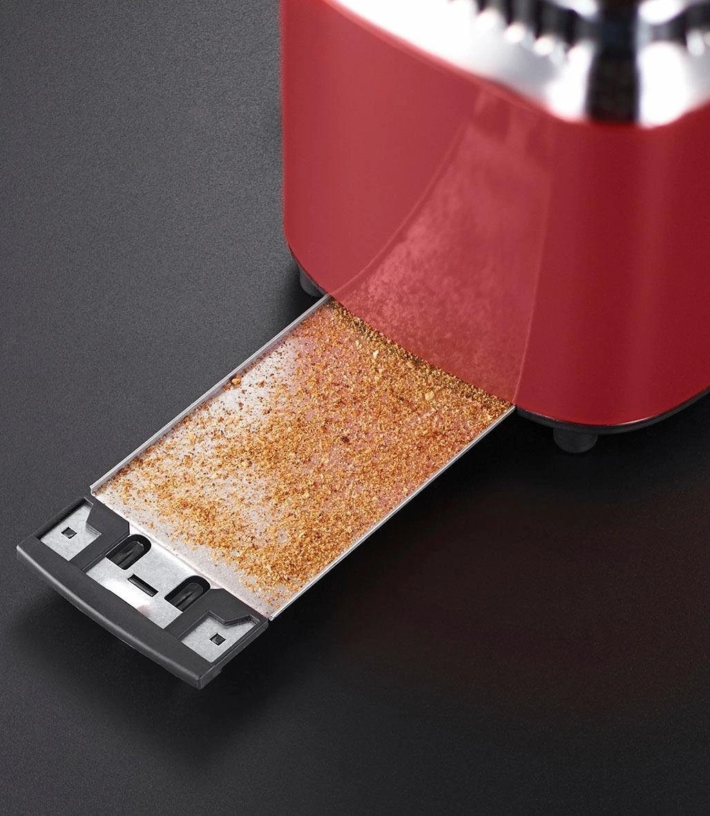 Nahaufnahme eines roten Toasters mit Krümelschublade, gefüllt mit Krümeln.
