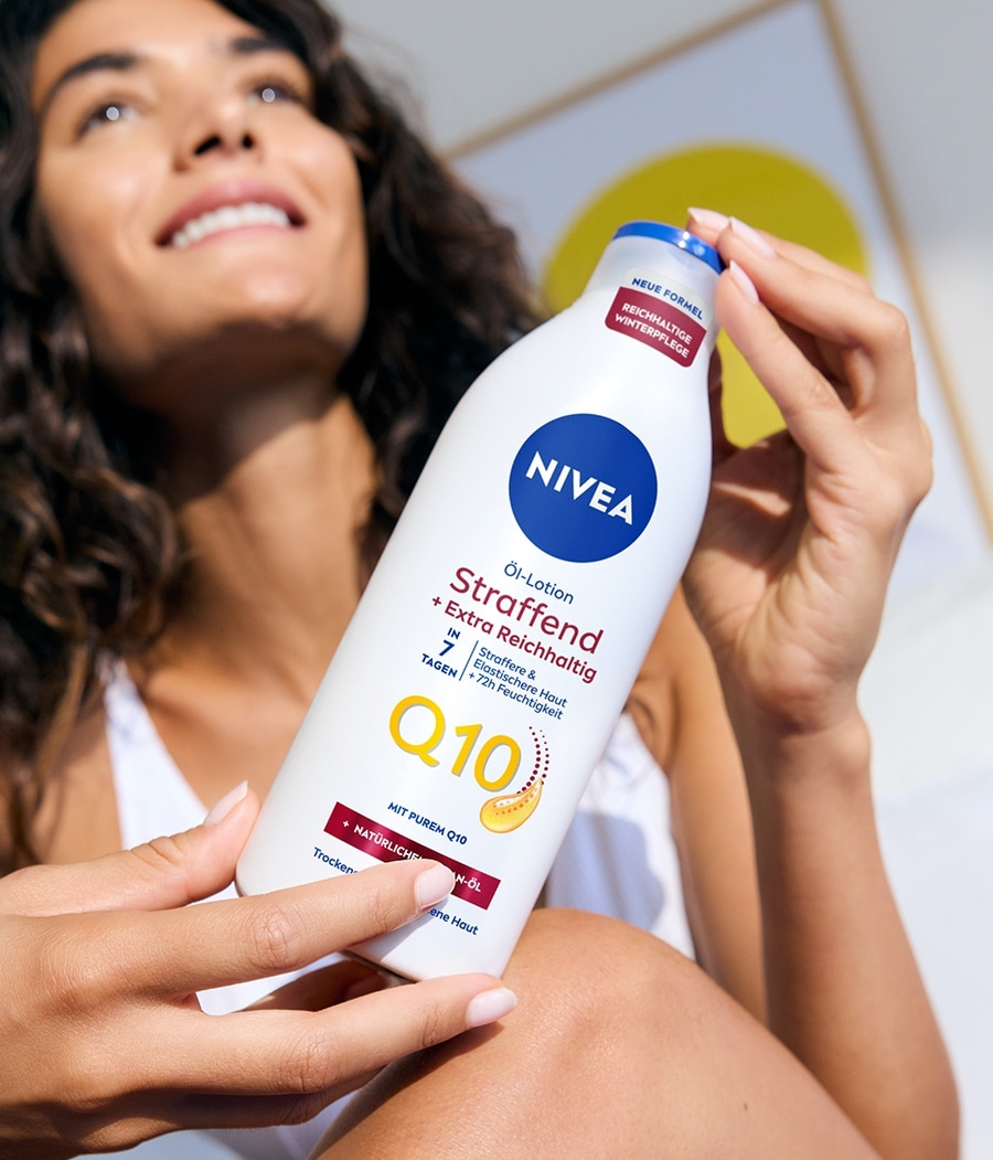 Frau hält Nivea Öl-Lotion Straffend. Q10, extra reichhaltig, Winterpflege, trockene Haut.