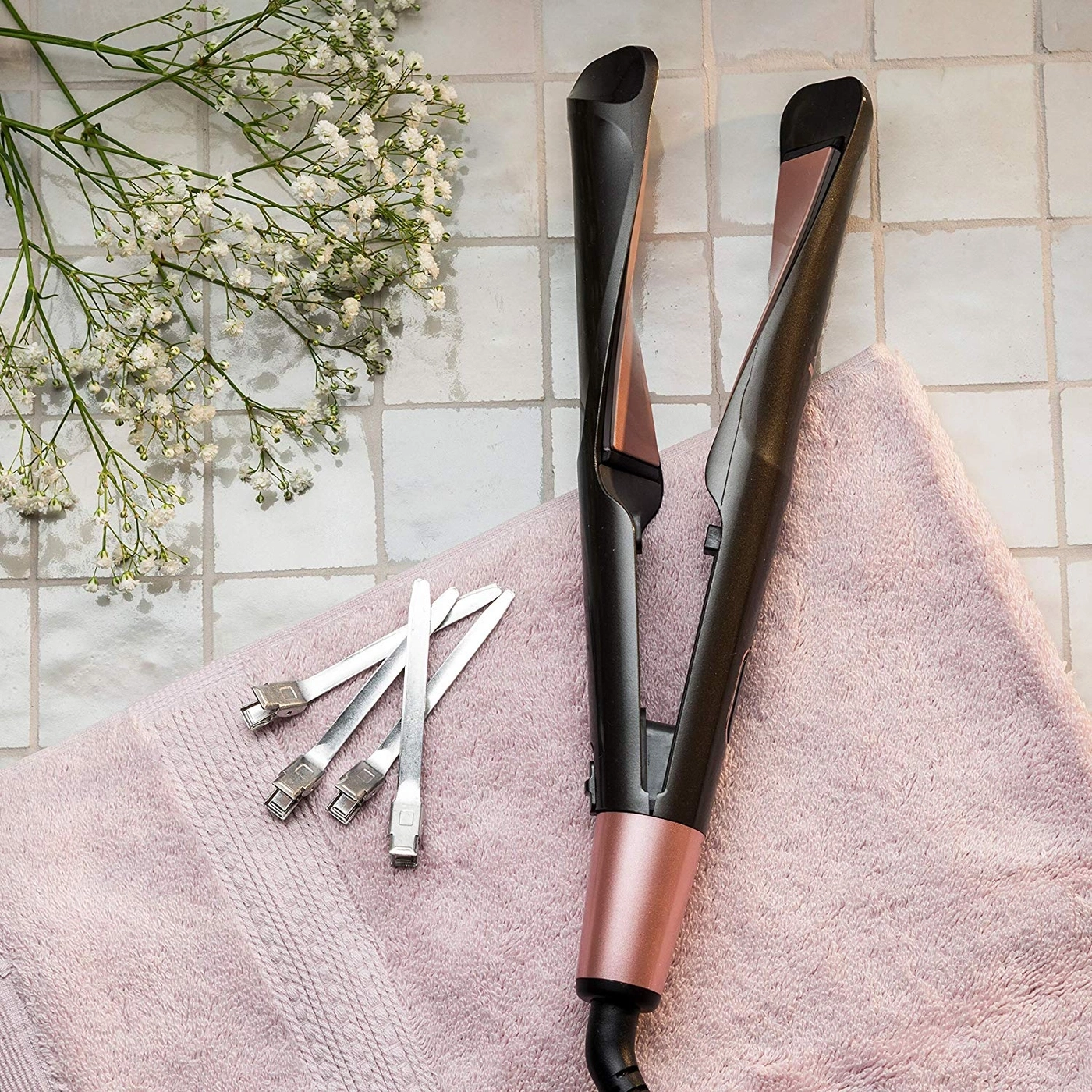Haarglätter, Handtuch, Blumen, Metallklammern auf Fliesenoberfläche