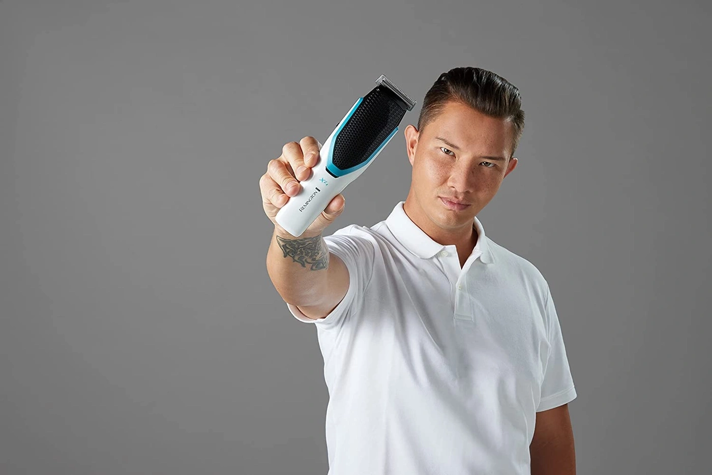 Mann hält Haarschneider. Er trägt ein weißes Polohemd. Grauer Hintergrund.