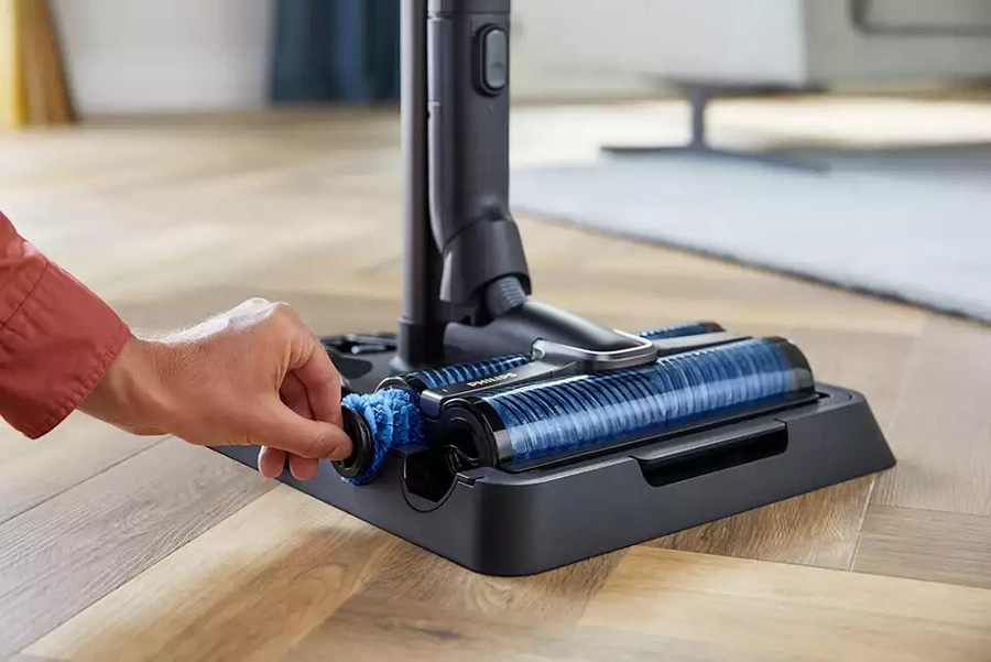 Person wechselt Bürste eines Staubsaugers, Nahaufnahme, blau, schwarz, Holz