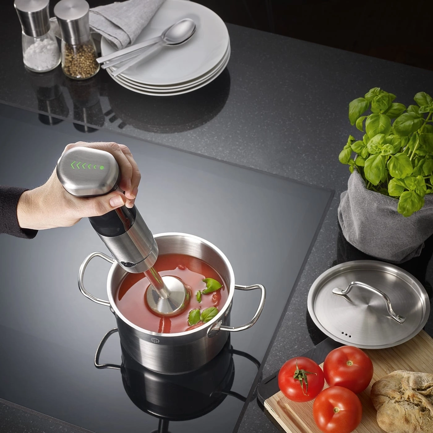 Hand taucht Stabmixer in Topf mit Tomatensuppe und Basilikum auf einem Induktionskochfeld