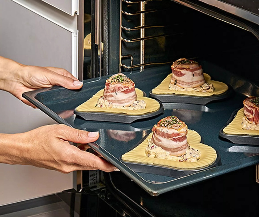 Person legt Tablett mit Fleisch in den Ofen, um es zu backen.