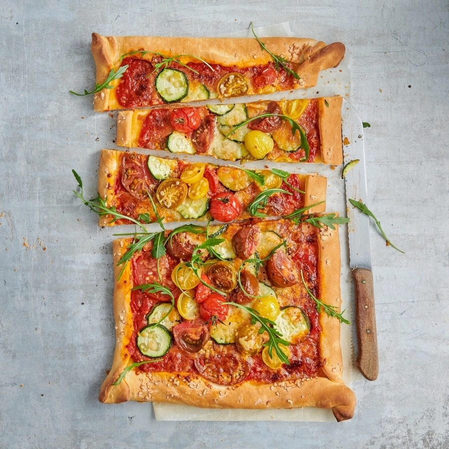 Pizza mit Tomaten, Zucchini und Rucola auf einem Backblech, geschnitten.