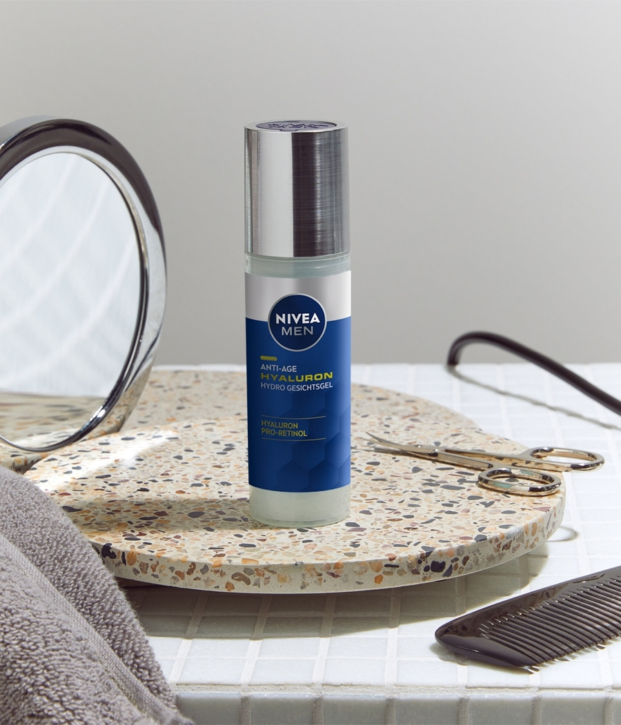 Nivea Men Anti-Age Hyaluron Hydro Gesichtsgel auf einer Ablage mit Spiegel, Schere und Kamm.